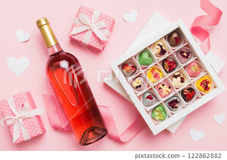 Bottle of red wine on colored background for Valentine Day with gift and chocolate. Heart shaped with gift box of chocolates top view with copy space Bottle of red wine on colored background for Valentine Day with gift and chocolate. Heart shaped with gift box of chocolates top view with copy space 122862882