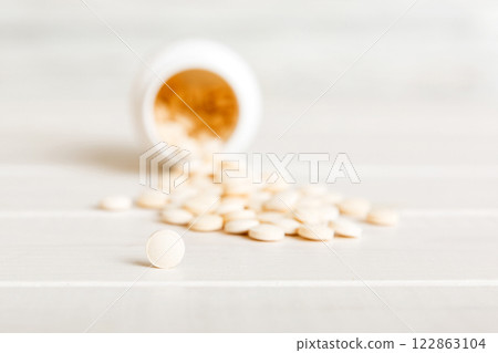 Medicine bottle and white pills spilled on a light background. Medicines and prescription pills flat lay background. White medical pills and tablets spilling out of a drug bottle Medicine bottle and white pills spilled on a light background. Medicines and prescription pills flat lay background. White medical pills and tablets spilling out of a drug bottle 122863104