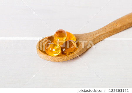 Vitamin omega capsules in a spoon on a colored background. Pills served as a healthy meal. Red soft gel vitamin supplement capsules on spoon 122863121
