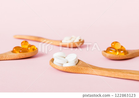Vitamin capsules in a spoon on a colored background. Pills served as a healthy meal. Red soft gel vitamin supplement capsules on spoon Vitamin capsules in a spoon on a colored background. Pills served as a healthy meal. Red soft gel vitamin supplement capsules on spoon 122863123