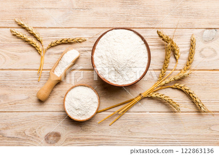 Flat lay of Wheat flour in wooden bowl with wheat spikelets on colored background. world wheat crisis Flat lay of Wheat flour in wooden bowl with wheat spikelets on colored background. world wheat crisis 122863136