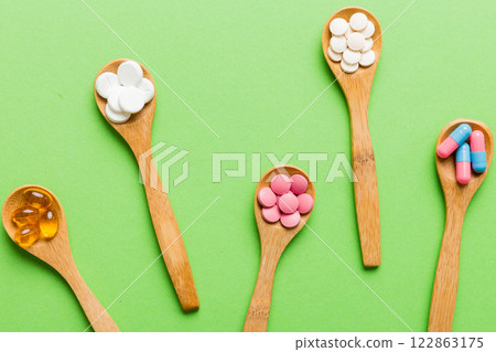 Vitamin capsules in a spoon on a colored background. Pills served as a healthy meal. Red soft gel vitamin supplement capsules on spoon 122863175