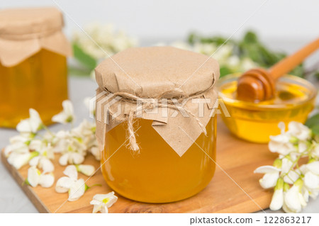 Sweet honey jar surrounded spring acacia blossoms. Honey flows from a spoon in a jar. jars of clear fresh acacia honey on wooden background Sweet honey jar surrounded spring acacia blossoms. Honey flows from a spoon in a jar. jars of clear fresh acacia honey on wooden background 122863217