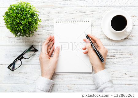Woman hand with pencil writing on notebook and hold coffee cup. Woman working on office table with coffee 122863265