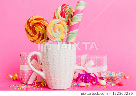 Colorful candies in cup on table on light background background. Large swirled lollipops. Creative concept of a jar full of delicious sweets from the candy store 122863289