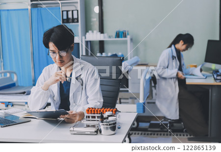 Positive doctor working on laptop in medical office, portrait. Positive doctor working on laptop in medical office, portrait. 122865139