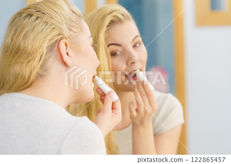 Woman in bathroom applying lip balm 122865457
