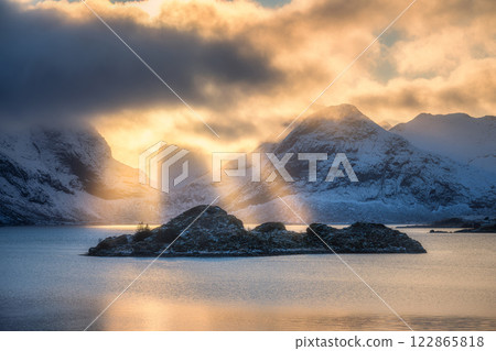 Snowy mountains in low clouds, bright golden sunbeams, fjord Snowy mountains in low clouds, bright golden sunbeams, fjord 122865818