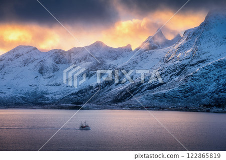 Snowy mountains in clouds, bright sunbeams, boat in fjord Snowy mountains in clouds, bright sunbeams, boat in fjord 122865819