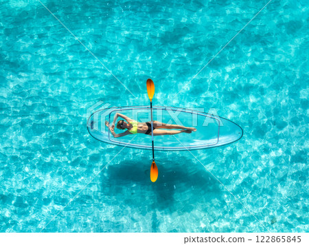 Aerial view of young woman lying on transparent canoe in blue se Aerial view of young woman lying on transparent canoe in blue se 122865845