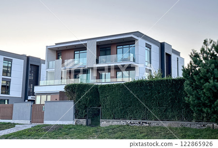 Modern luxury house with glass balconies, large windows, and green landscaping 122865926