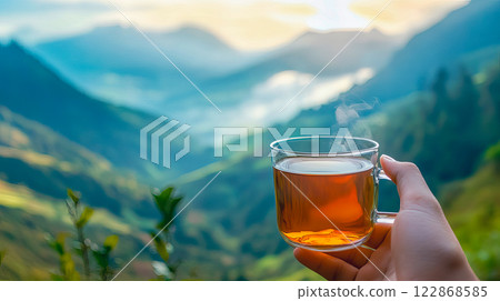 Close-up of cup with tea in travelers hand with a view of nature and mountains 122868585