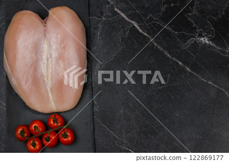 The chicken breast fillet lies on a black board on a dark background with a sprig of tomatoes next to the text space. The concept of proper and healthy nutrition, dietary dishes and recipes. High The chicken breast fillet lies on a black board on a dark background with a sprig of tomatoes next to the text space. The concept of proper and healthy nutrition, dietary dishes and recipes. High 122869177