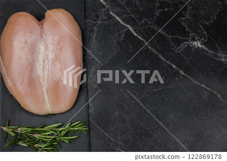 Chicken breast fillet lying on a black board on a dark background with a sprig of rosemary on a dark background with space for text. The concept of proper and healthy nutrition, dietary dishes and 122869178