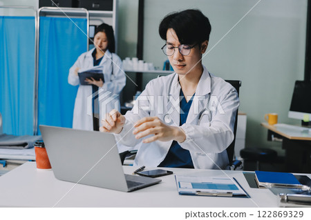 Positive doctor working on laptop in medical office, portrait. 122869329