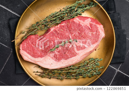 Raw Striploin steak, New York strip beef steak in a plate with herbs. black background. top view 122869851