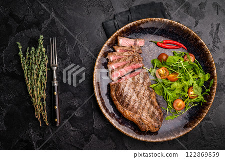 Grilled striploin steak, beef meat steak on a plate with salad. black background. top view Grilled striploin steak, beef meat steak on a plate with salad. black background. top view 122869859