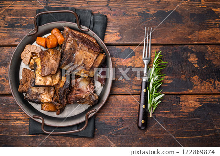 Grilled beef short ribs glistening under natural light, accompanied by fresh greens and spices, capturing the essence of gourmet comfort food. wooden background. top view 122869874