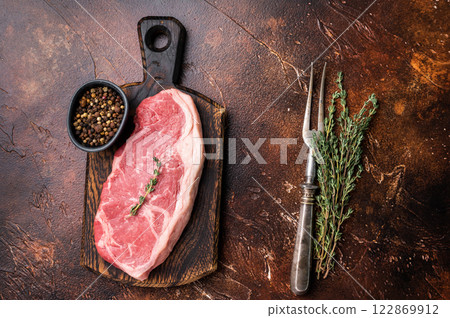 Raw New York strip beef steak, also named Striploin steak on a wooden board. brown background. top view Raw New York strip beef steak, also named Striploin steak on a wooden board. brown background. top view 122869912