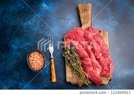 Beautifully sliced raw buffalo meat on a rustic platter, showcasing its appealing color and quality, perfect for grilling or roasting. blue background. top view Beautifully sliced raw buffalo meat on a rustic platter, showcasing its appealing color and quality, perfect for grilling or roasting. blue background. top view 122869921