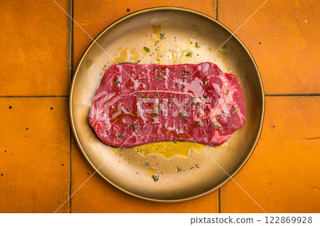 Marinated with olive oil and herbs Raw top sirloin or rump beef steak. orange background. top view Marinated with olive oil and herbs Raw top sirloin or rump beef steak. orange background. top view 122869928