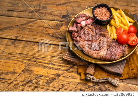 A juicy Grilled Chuck eye roll steak and garnish with french fry on a plate. wooden background. top view A juicy Grilled Chuck eye roll steak and garnish with french fry on a plate. wooden background. top view 122869935