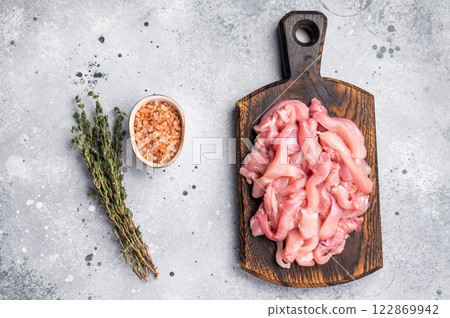 Raw sliced Chicken meat, strips fillets on wooden board. grey background. top view Raw sliced Chicken meat, strips fillets on wooden board. grey background. top view 122869942