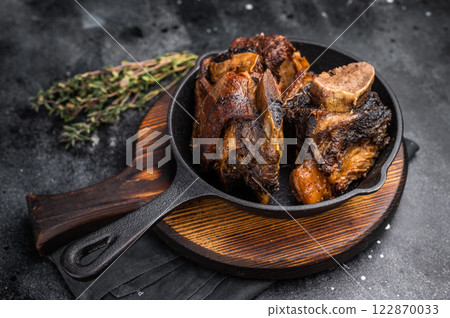 Tender beef short ribs in a pan, seasoned with herbs and spices. Perfect for culinary blogs or restaurant menus that focus on hearty, flavorful meat dishes. black background. top view 122870033