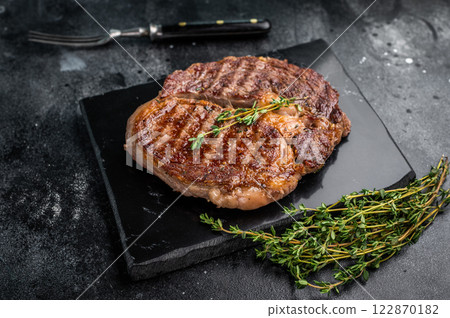 Rib eye steak with herbs on marble board, grilled prime beef meat. black background. top view Rib eye steak with herbs on marble board, grilled prime beef meat. black background. top view 122870182