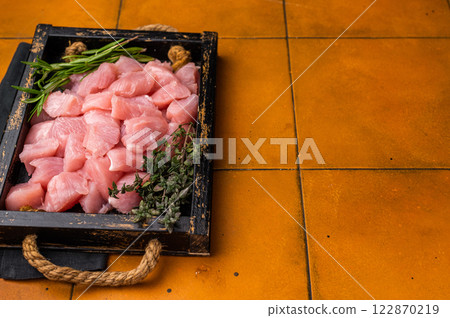 Diced sliced chicken fillet cubes, poultry meat with herbs for cooking. orange background. top view Diced sliced chicken fillet cubes, poultry meat with herbs for cooking. orange background. top view 122870219