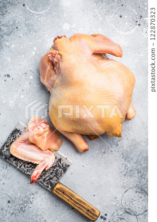 A whole raw chicken sits next to a chicken wing on a butcher's block 122870323