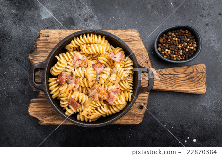 Fusilli carbonara pasta topped with crispy bacon bits and parmesan cheese in a skillet. Black background. Top view Fusilli carbonara pasta topped with crispy bacon bits and parmesan cheese in a skillet. Black background. Top view 122870384