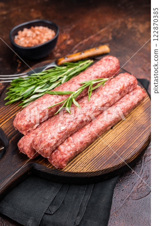 Fresh raw beef and lamb meat kebabs sausages on wooden board. brown background. top view Fresh raw beef and lamb meat kebabs sausages on wooden board. brown background. top view 122870385