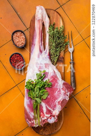 Whole raw lamb leg, uncooked mutton meat on butcher board. orange background. top view 122870469