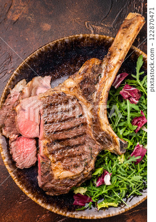 Grilled and sliced Tomahawk beef steak, marble rib eye with bone on plate with salad. brown background. top view Grilled and sliced Tomahawk beef steak, marble rib eye with bone on plate with salad. brown background. top view 122870471