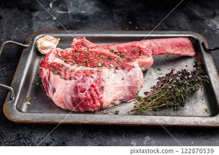 Ready for cooking Tomahawk beef steak with seasonings, raw marbled rib eye with bone on steel tray. black background. top view Ready for cooking Tomahawk beef steak with seasonings, raw marbled rib eye with bone on steel tray. black background. top view 122870539