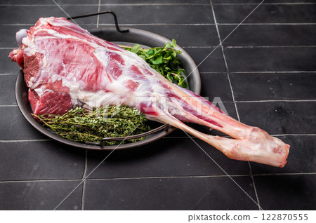Uncooked whole goat leg, raw meat with herbs for cooking. black background. top view 122870555