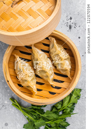 Steamed Jiaozi Chinese Dumplings with meat and vegetables in bamboo steamer. grey background. top view Steamed Jiaozi Chinese Dumplings with meat and vegetables in bamboo steamer. grey background. top view 122870594