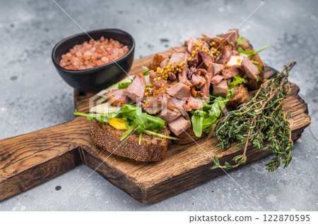Open sandwich with duck fillet meat, foie gra liver, arugula and cheese on board. grey background. top view Open sandwich with duck fillet meat, foie gra liver, arugula and cheese on board. grey background. top view 122870595