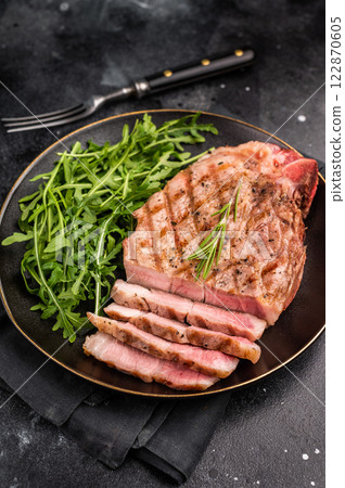 BBQ grilled pork tender steak, neck meat, on plate with salad. black background. top view BBQ grilled pork tender steak, neck meat, on plate with salad. black background. top view 122870605