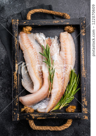 Ready for cooking Raw Hake fish fillets in a wooden tray with herbs. black background. top view Ready for cooking Raw Hake fish fillets in a wooden tray with herbs. black background. top view 122870609