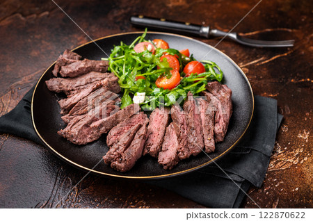 Grilled and sliced Beef Denver strip Steak on a plate with salad. brown background. top view 122870622