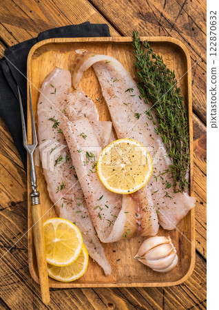 Raw Pollock and Hake fish fillets on a wooden board with herbs ready for cooking. wooden background. top view 122870632