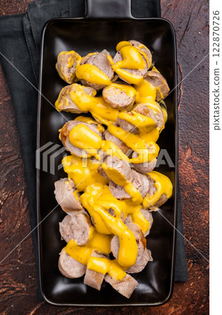BBQ Grilled and sliced Sausages with cheese and mustard sauce in plate. brown background. top view BBQ Grilled and sliced Sausages with cheese and mustard sauce in plate. brown background. top view 122870726