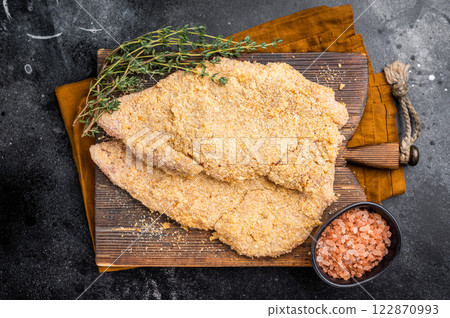 Wiener breaded raw pork Schnitzel, meat steak on a wooden board. black background. top view 122870993