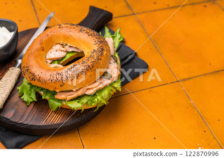 Breakfast Bagel with smoked salmon, lettuce and cream cheese on a wooden board. orange background. top view Breakfast Bagel with smoked salmon, lettuce and cream cheese on a wooden board. orange background. top view 122870996