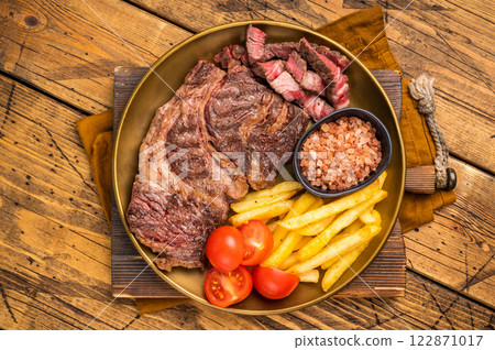 A juicy Grilled Chuck eye roll steak and garnish with french fry on a plate. wooden background. top view 122871017