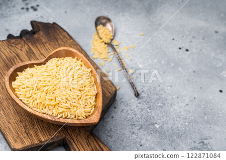 Raw Orzo pasta, uncooked dry Italian risoni in a bowl. grey background. top view Raw Orzo pasta, uncooked dry Italian risoni in a bowl. grey background. top view 122871084