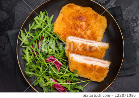 Chicken cordon bleu cutlet with cheese and ham on plate with salad. black background. top view Chicken cordon bleu cutlet with cheese and ham on plate with salad. black background. top view 122871086