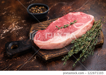 Raw New York strip beef steak, also named Striploin steak on a wooden board. brown background. top view Raw New York strip beef steak, also named Striploin steak on a wooden board. brown background. top view 122871103